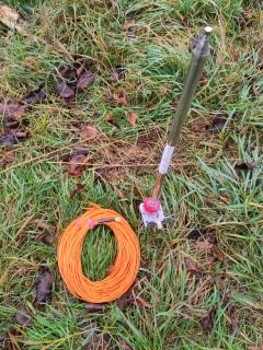 im Gras liegt eine Rolle orangener Draht, daneben steckt eine Teleskopantenne im Boden